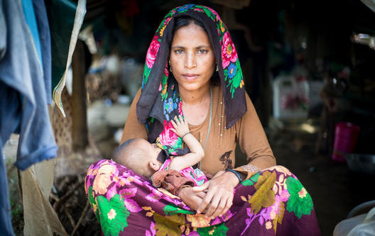 Portrait of Lal Moti 35 and Osmaitara 3 months in Kutupalong Refugee Camp in Bangladesh. ; As an estimated 621,000 people sought safety in Bangladesh between late-August and November 2017, UNHCR doubled its efforts to provide shelter in and around existing camps near Cox’s Bazar. Whole families, young mothers and unaccompanied minors were among those fleeing for their lives when fighting reignited in Myanmar. They came by boat or walked barefoot for days, wading through vast rice fields. They left most of their possessions behind. Large groups crossed into south-eastern Bangladesh hungry, traumatised, in poor physical condition and in need of life-saving support. UNHCR is working with the Bangladesh Government to provide Rohingya refugees with protection, food, clean water, shelter, health care, trauma counselling and reunification for separated families. Portrait of woman with 3 months old baby in Refugee Camp in Bangladesh.